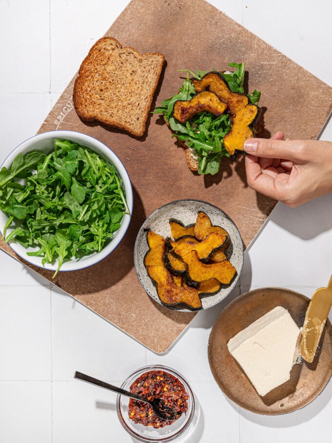 hand placing roasted squash on sandwich